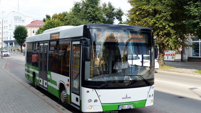 Ilustracja przedstawia biało-zielony autobus komunikacji miejskiej stojący w zatoczce przy przystanku. Przystanek znajduje się przy ulicy Mickiewicza w Bielsku Podlaskim. W tle widać budynki Urzędu Miasta i Starostwa Powiatowego.