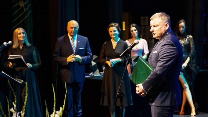 Ilustracja przedstawia burmistrza Jarosława Borowskiego (z prawej strony kadru) na scenie opery, przemawiającego do mikrofonu. W tle stoi 5 osób: organizatorzy i prowadzący galę.