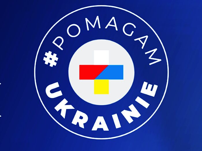 Ilustracja przedstawia okrągłe logo. Na niebieskim tle okrągły biały napis "Pomagam Ukrainie", a w środku skrzyżowane barwy z flag: polskiej i ukraińskiej.