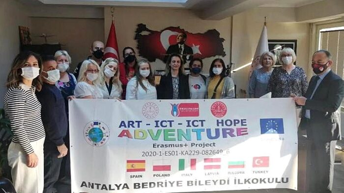 Ilustracja przedstawia grupę stojących osób - uczestników programu. Osoby te trzymają baner reklamowy z nazwą projektu, flagami uczestniczących w nim państw oraz napisem w języku tureckim.