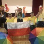 Dzieci w scenicznych przebraniach z polską flagą i tęczowymi parasolkami.