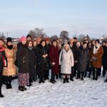 Pamiątkowe zdjęcie uczestników spotkania na promenadzie w parku przy ul. Jagiellońskiej. Kilkudziesiecioosobowa grupa ludzi ubranych w zimowe stroje uśmiecha się do obiektywu. Promenadę pokrywa świeży śnieg.