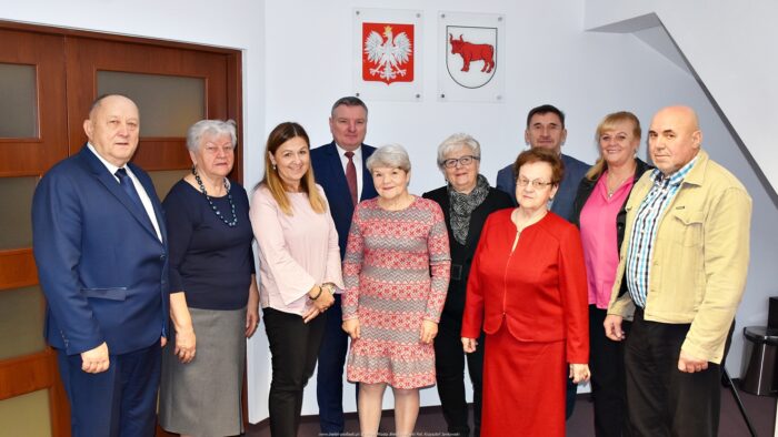 Dziesięć osób stoi w grupie - to członkowie rady seniorów, w towarzystwie burmistrza i dwojga pracowników urzędu. Wszyscy pozują do obiektywu. W tle biała ściana sali konferencyjnej, drzwi oraz godło Polski i herb miasta Bielsk Podlaski.