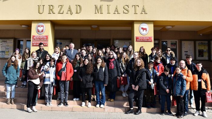 Grupa ponad 50 osób - uczestników spotkania w ramach programu Erasmus. Młodzież i dorośli w zimowych ubraniach stoją na schodach urzędu miasta. Nad nimi widać duży napis zawieszony na ścianie "urząd miasta". Wszyscy pozują do zdjęcia.