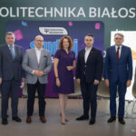 Siedem osób dorosłych stoi w rzędzie i pozuje do zdjęcia. W tle napis "Politechnika Białostocka" i rolapy reklamowe.