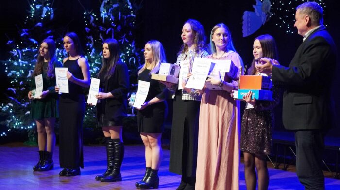 Siedem młodych kobiet - laureatek najstarszej kategorii wiekowej - stoi w rzędzie na scenie i prezentuje otrzymane dyplomy i nagrody. Z prawej burmistrz spogląda na nie z uśmiechem i klaszcze.