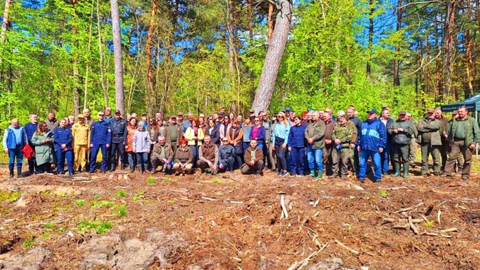 Grupa kilkudziesięciu dorosłych osób, uczestników akcji, toi na tle lasu.