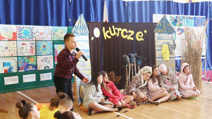 Kilkoro dzieci przedstawia teatrzyk. W tle wywieszone plakaty konkursowe i napis "O kurczę".