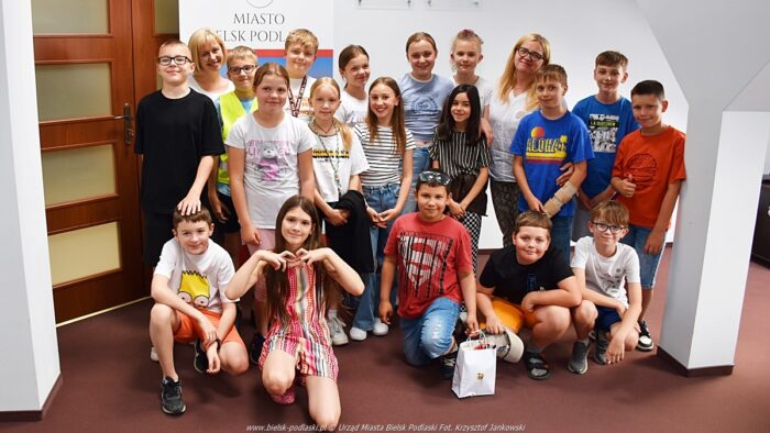 Grupowe zdjęcie kilkunastu uczniów z panią zastępcą burmistrza i z nauczycielką. W tle godło Polski i herb miasta.