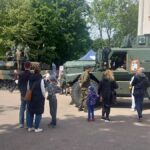 Czołg i wóz opancerzony na placu szkolnym. Wokół osoby oglądające prezentowany sprzęt wojskowy.