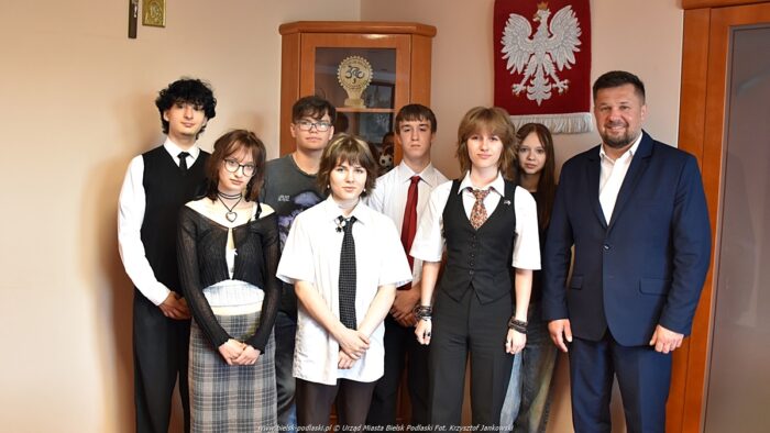 Osiem osób stoi w gabinecie burmistrza i pozuje do zdjęcia. Z prawej burmistrz, obok przedstawiciele młodzieży. W tle godło Polski.