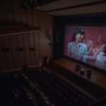 Ciemne wnętrze sali kinowej. Po prawej widać ekran z wyświetlanym na nim kadrem z filmu.