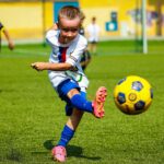 Sześcioletnie dzieci w strojach sportowych grają w piłkę na zielonej sztucznej murawie bielskiego stadionu.