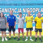 Młodzi ludzie w strojach sportowych stoją w rzędzie i pozują do zdjęcia. W tle baner z informacją o finansowaniu zawodów przez Miasto Bielsk Podlaski.