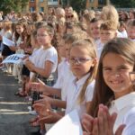 Duża grupa dzieci stojących w kilku szeregach i klaszczących podczas uroczystości rozpoczęcia roku szkolnego.