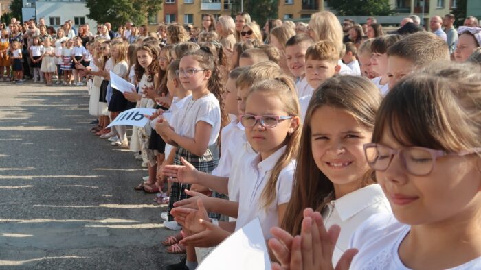 Duża grupa dzieci stojących w kilku szeregach i klaszczących podczas uroczystości rozpoczęcia roku szkolnego.