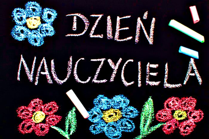 Grafika symbolizuje tablice szkolną o czarnym tle, z napisem "Dzien nauczyciela" oraz narysowanymi kolorową kredą czterema kwiatkami.