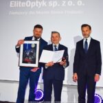 Grupa osób pozuje do grupowego zdjęcia na scenie.