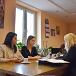 Trzy kobiety siedzą za stołem w gabinecie i rozmawiają.