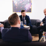 Trzech mężczyzn i kobieta siedzą wokół stolika i rozmawiają.