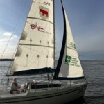 Jezioro i żaglówka z logotypami miasta i hufca na żaglu.