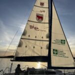 Jezioro i żaglówka z logotypami miasta i hufca na żaglu.