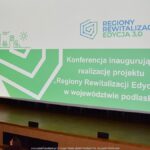 Scena domu kultury z ekranem, na którym wyświetlana jest plansza z nazwą konferencji.