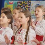 Śpiewający zespół szkolny - dziewczęta obrane w biało-czerwone stroje ludowe.