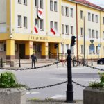 Kolorowe kwiaty miejskich nasadzeń. W tle skrzyżowanie i urząd miasta.