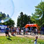 Zawody w nordic walkingu w lesie. Na pierwszym planie latające bańki mydlane, w tle odbywające się zawody.