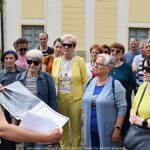 Grupa osób spacerujących po mieście z przewodniczką PTTK.