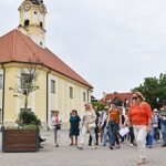 Grupa osób spacerujących po mieście z przewodniczką PTTK.