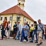 Grupa osób spacerujących po mieście z przewodniczką PTTK.