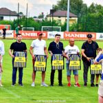 Grupa mężczyzn podczas uroczystości na boisku - odbiera pamiątkowe tablice z koszulkami.