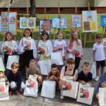 Święto skweru. Dzieci pozujące przed swoimi pracami plastycznymi wystawionymi na sztalugach.