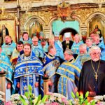 Wspólne zdjęcie duchownych w kolorowych strojach liturgicznych, na tle wnętrza cerkwi.