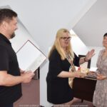 Mężczyzna i dwie kobiety podczas wręczania podziękowań i gratulacji.