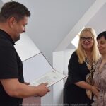 Mężczyzna i dwie kobiety podczas wręczania podziękowań i gratulacji.