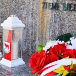 Kwiaty i znicz przed pomnikiem.