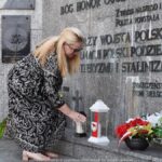 Kobieta ustawia znicz przed pomnikiem.