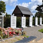 Widok na upamiętnienie na cmentarzu wojennym - Polską Drogę Krzyżową - składającą się z kilkunastu tablic ustawionych w szeregu.