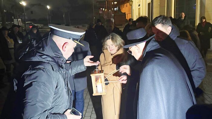 Uroczystość przekazania ognia z Betlejem przed ratuszem. Harcerze, księża i osoby cywilne zapalają łuczywa od ognia.
