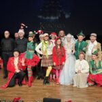 Grupa aktorów pozujących do grupowego zdjęcia na scenie.