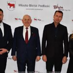 Uśmiechnięci ludzie w trakcie powitania na tle ścianki.