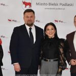 Uśmiechnięci ludzie w trakcie powitania na tle ścianki.