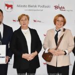 Uśmiechnięci ludzie w trakcie powitania na tle ścianki.