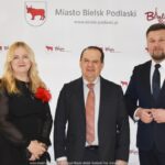 Uśmiechnięci ludzie w trakcie powitania na tle ścianki.