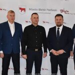 Uśmiechnięci ludzie w trakcie powitania na tle ścianki.