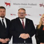 Uśmiechnięci ludzie w trakcie powitania na tle ścianki.