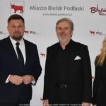 Uśmiechnięci ludzie w trakcie powitania na tle ścianki.